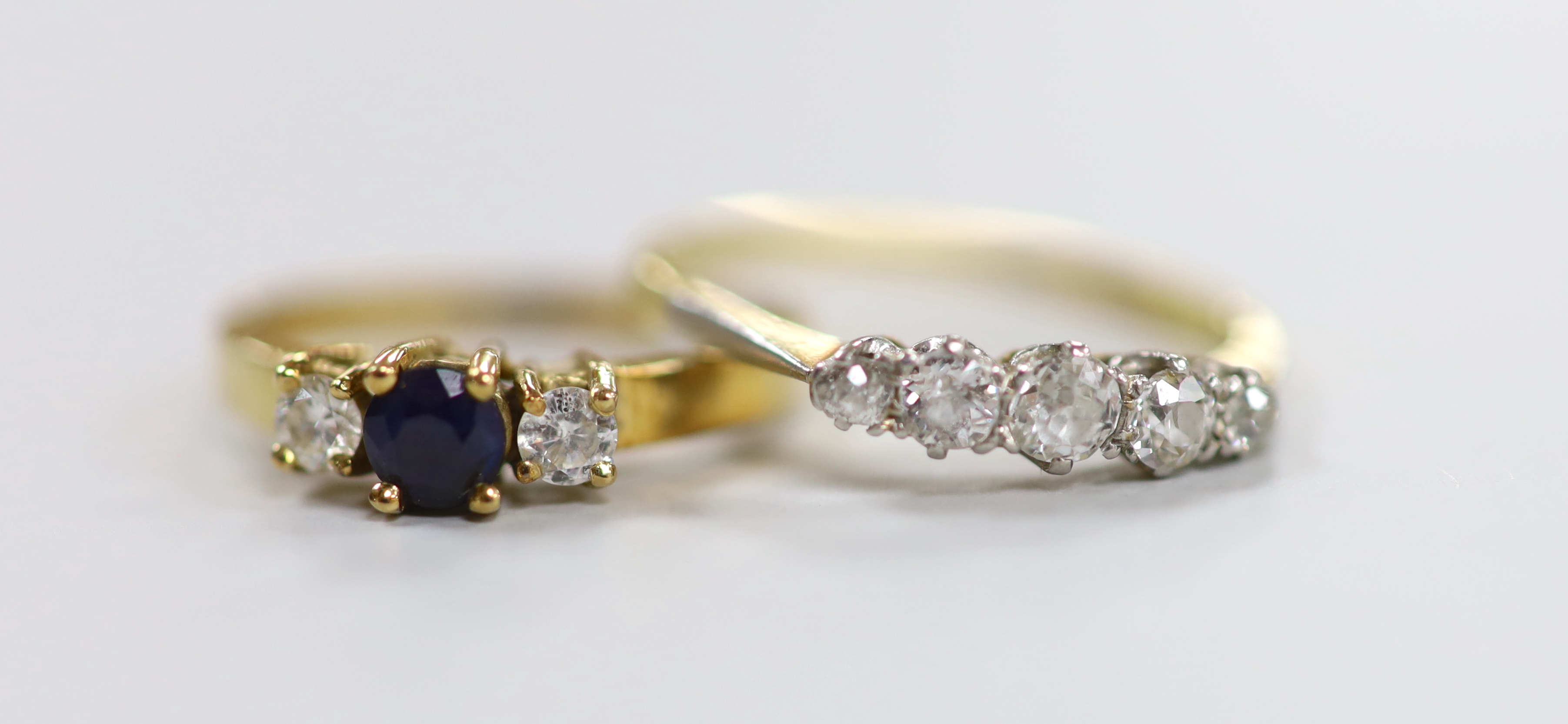 An 18ct, plat and graduated five stone diamond set half hoop ring, size N/O, gross weight 2.1 grams and a 585 yellow metal, sapphire and diamond set three stone ring, 2.2 grams.